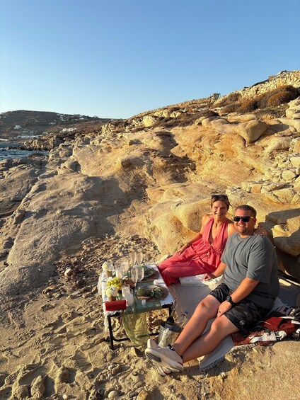 A couple sitting on a beach with a picnic setup. 5