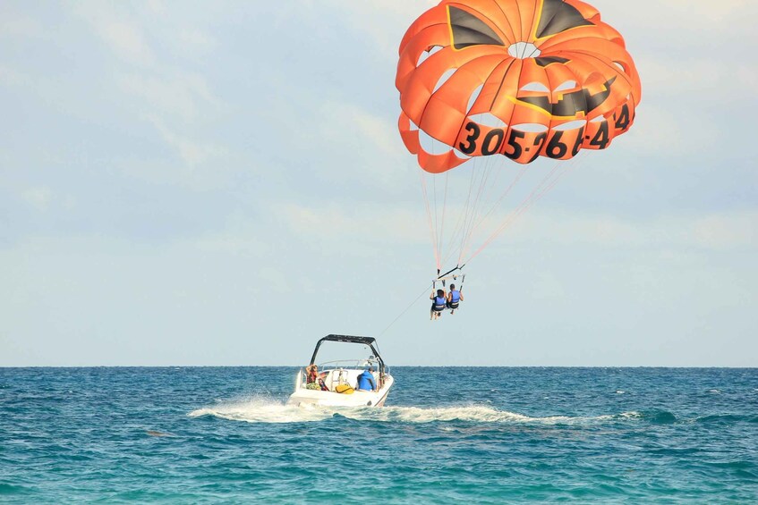 A parasail with the number 305-761-4 in the sky, a boat creating a wake, and the ocean in the background. 4