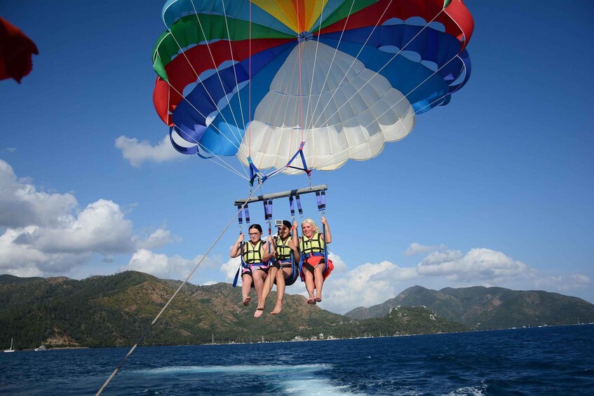 A parasailing activity with three individuals in life jackets, a colorful parachute, and a mountainous landscape in the background. 1