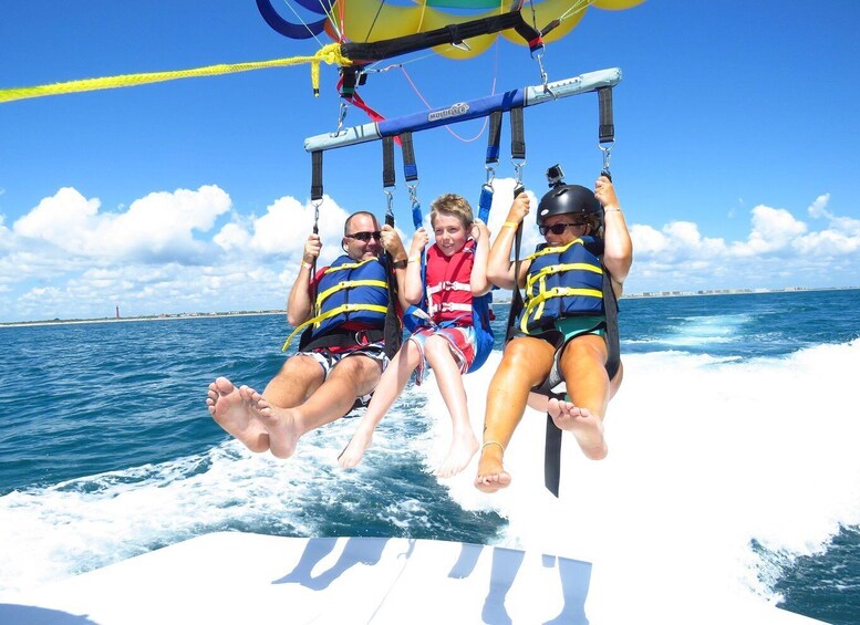 Three people on a watercraft with a parasail, ocean, and a lighthouse in the background. 3