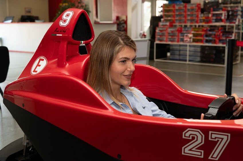 A person in a red go-kart with the number 27, inside a building with shelves in the background. 3
