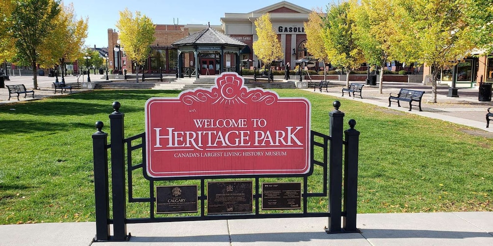 A welcome sign for Heritage Park, a living history museum, with a plaque and a building in the background. 1