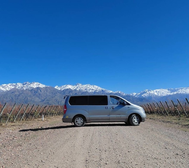 A silver minivan parked on a gravel road with a mountain range in the background. 2