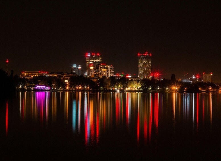 A nighttime cityscape with illuminated buildings reflected in a calm body of water. 3