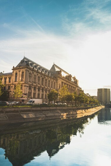 A large, historic building with a reflection in the water, surrounded by trees and a clear sky. 1