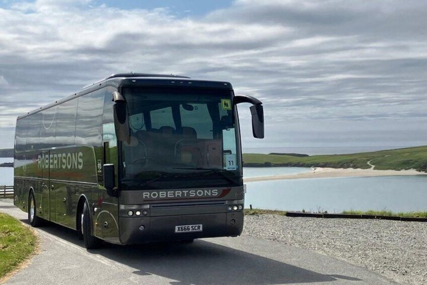 A black bus with 'ROBERTSONS' on the side, driving on a road with a lake and hills in the background. 2