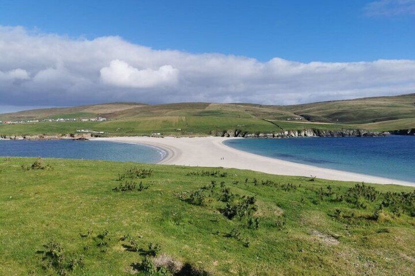 A coastal landscape with a sandy beach, grassy areas, and a clear blue sky. 4