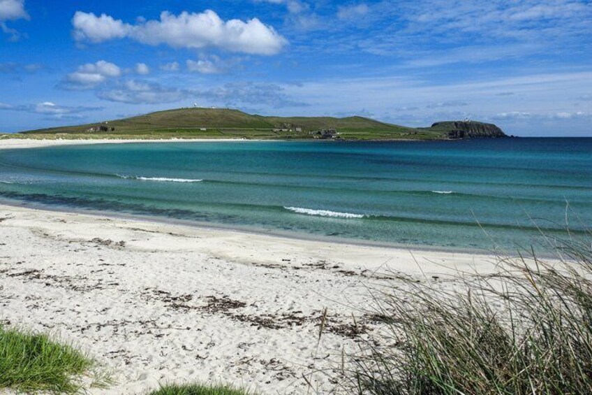 A beach with clear turquoise water, white sand, and grassy dunes. 3