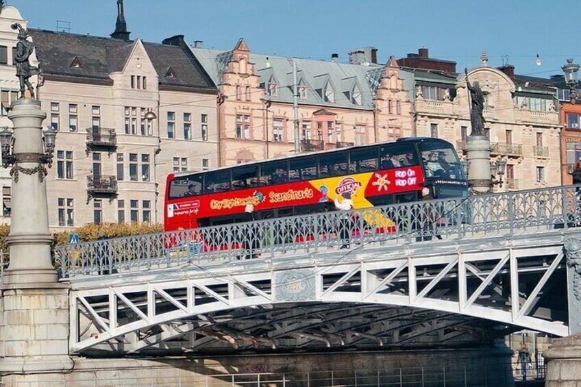 A red double-decker bus on a bridge with ornate buildings in the background. 3