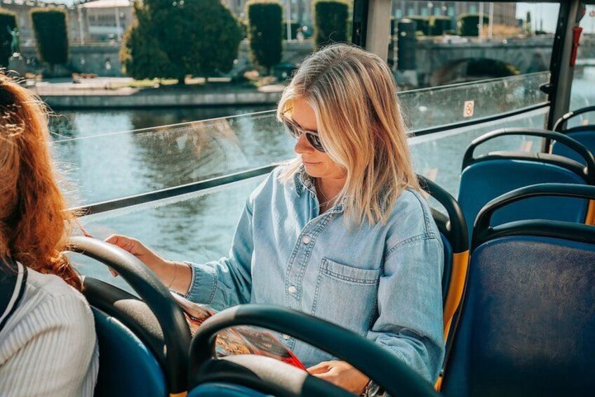 En person som kör en buss, med en flod och byggnader i bakgrunden. 5