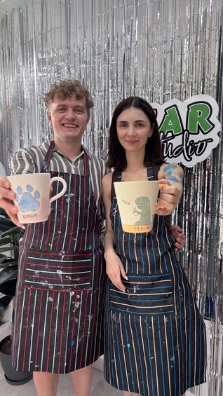 Two people holding mugs with animal prints, standing in front of a shiny silver backdrop with a sign that reads 'AR'. 3