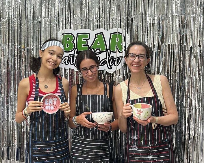 Four people in striped aprons holding bowls with text, standing in front of a silver backdrop with the words 'BEAR and love' visible. 5