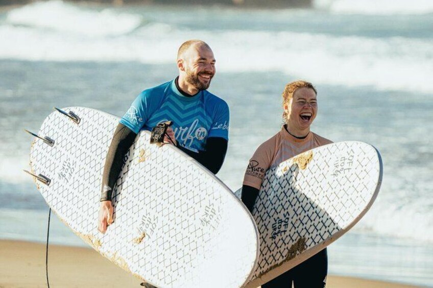 Two people holding surfboards on a beach with waves in the background. 3