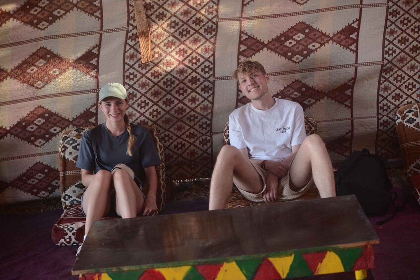 Two people sitting on patterned rugs with a wooden table in front. 5