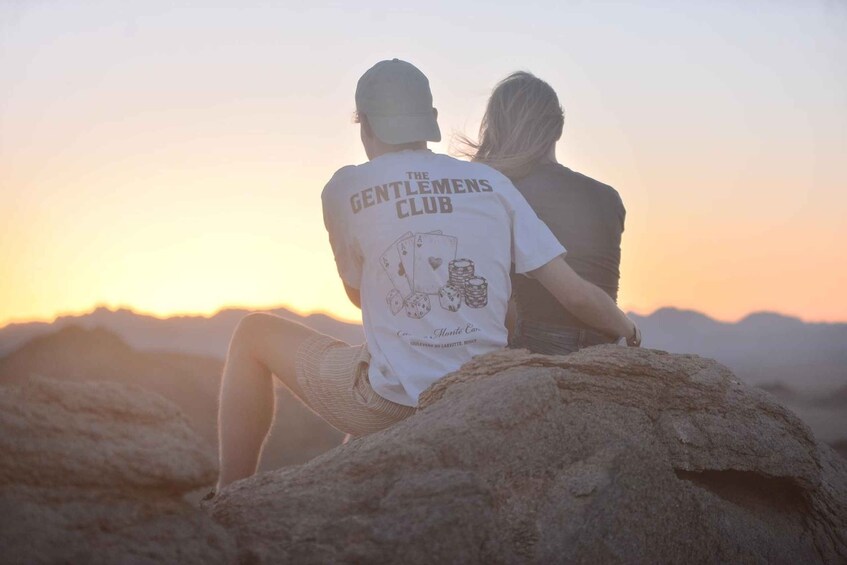 Two people sitting on a rock with a sunset in the background. 3