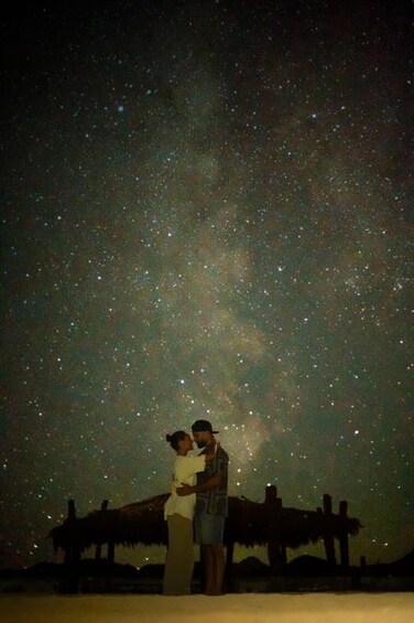 Two people embracing under a starry night sky with a wooden structure in the background. 1