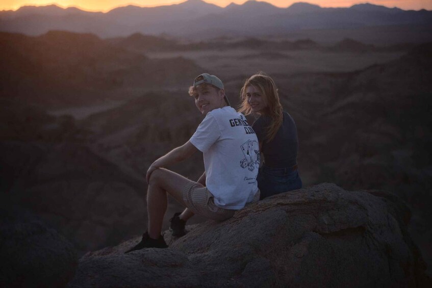 Two people sitting on a rock with a mountainous landscape in the background. 4