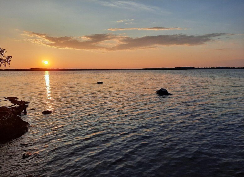 A sunset over a calm body of water with rocks and a distant shoreline. 4