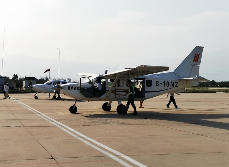 A small white aircraft with 'B-10NZ' on its side parked on a tarmac with another aircraft in the background. 5