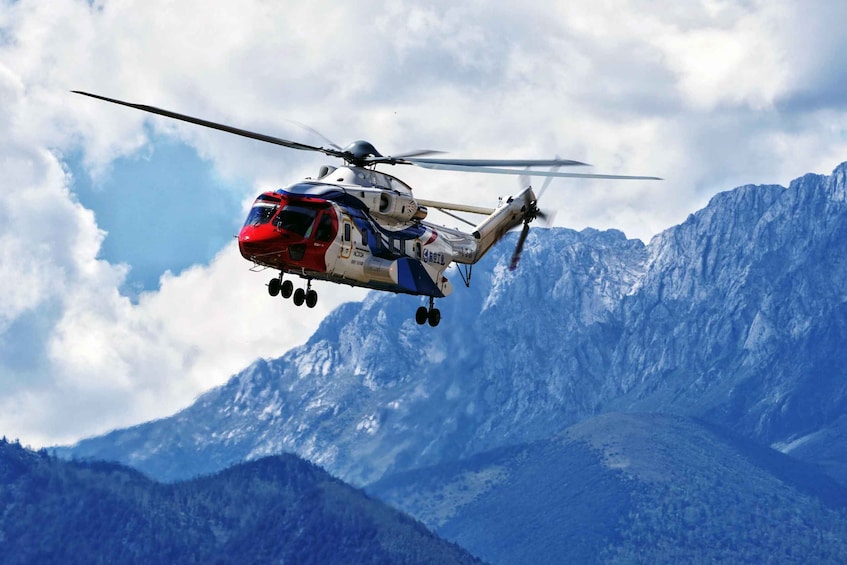 A red and white helicopter flying over a mountainous landscape. 1