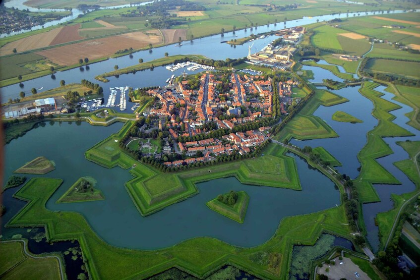 An aerial view of a town with a central water body, surrounded by green fields and a fortified structure. 1