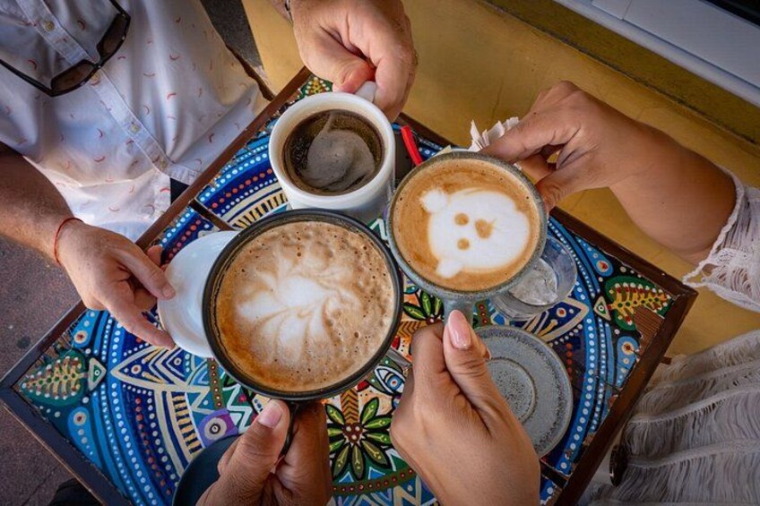 Three people holding cups of coffee with latte art on a colorful table. 3