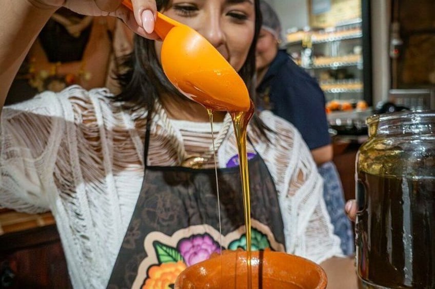 A person pouring a yellow liquid from an orange spoon into a bowl. 2