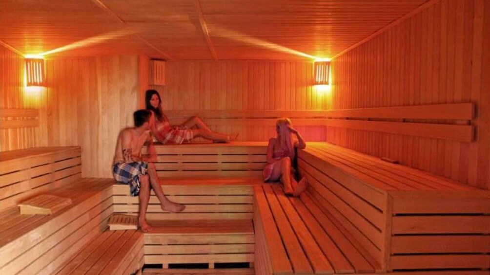 A sauna with wooden benches and walls, and two people sitting on them. 1