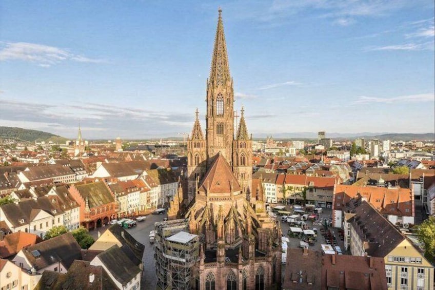 A cathedral with a tall spire, surrounded by a town with red-roofed buildings. 1