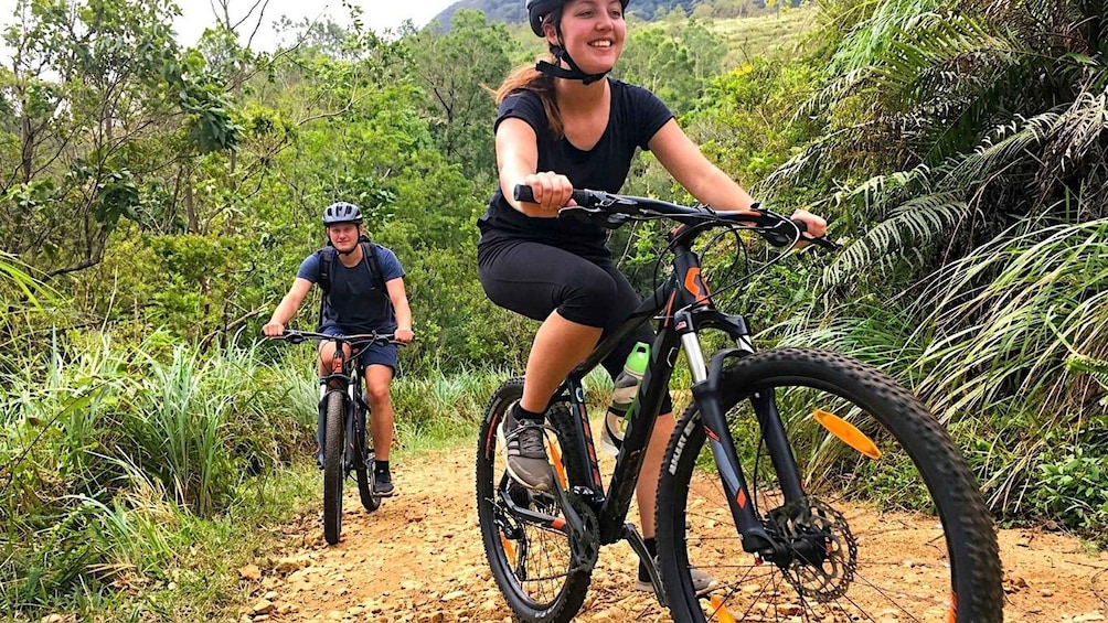 Two cyclists on a dirt trail surrounded by lush greenery. 1