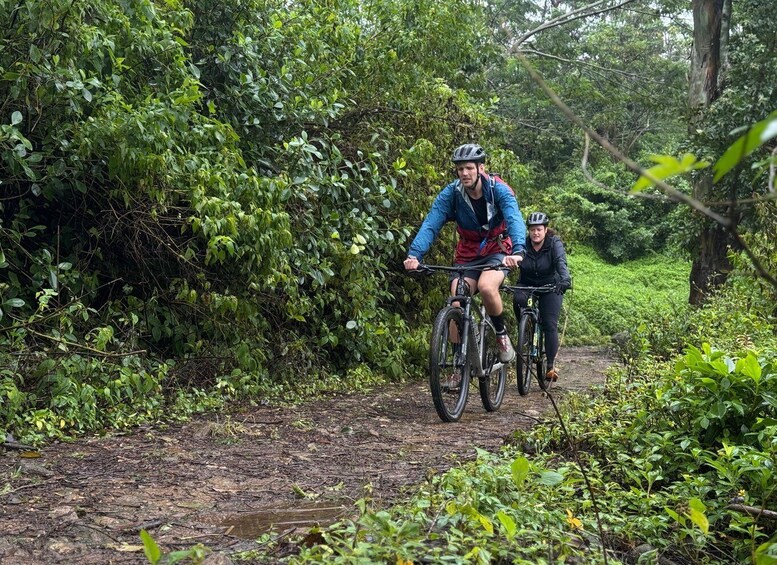 Two cyclists on a muddy trail surrounded by dense greenery. 2