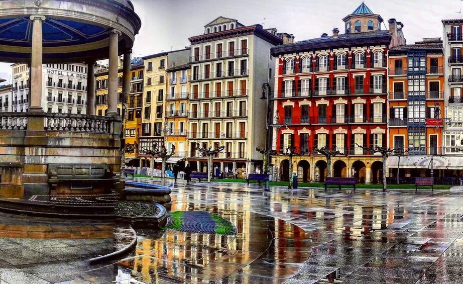 A historic square with a fountain, reflecting buildings, and a covered structure. 1