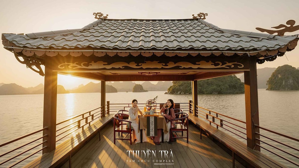 A wooden boat with a traditional roof, a table with chairs, and a view of a calm lake with distant islands. 2