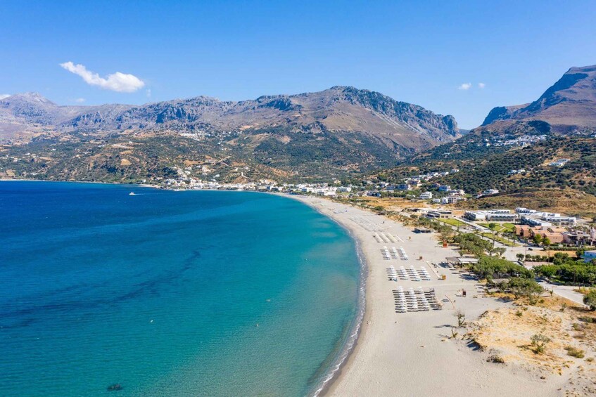 A coastal town with a beach, mountains, and clear blue sea. 1