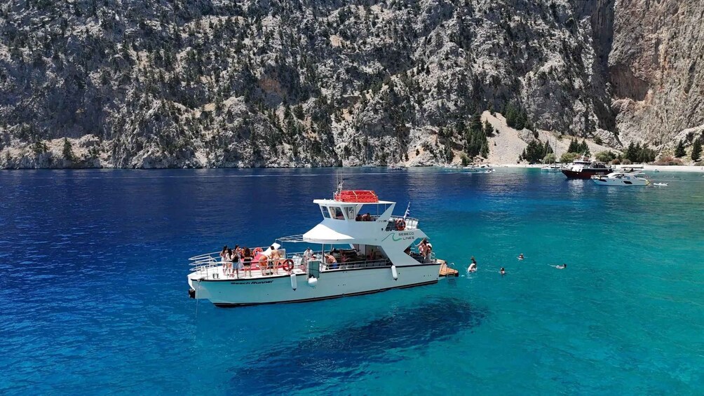 A white boat named 'Beach Runner' with people on board and swimming in the water, surrounded by clear blue sea and rocky cliffs. 3