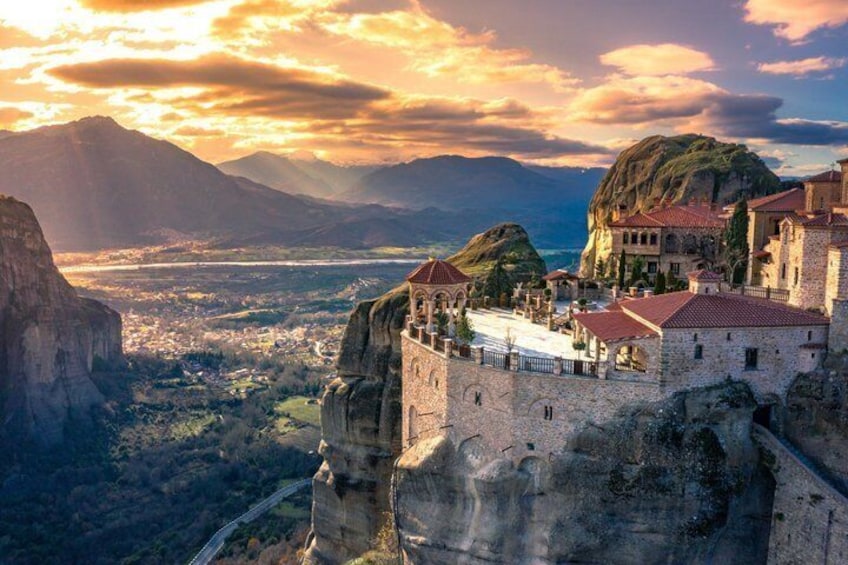 A historic stone fortress on a cliff overlooking a valley, with a river and mountains in the background. 1