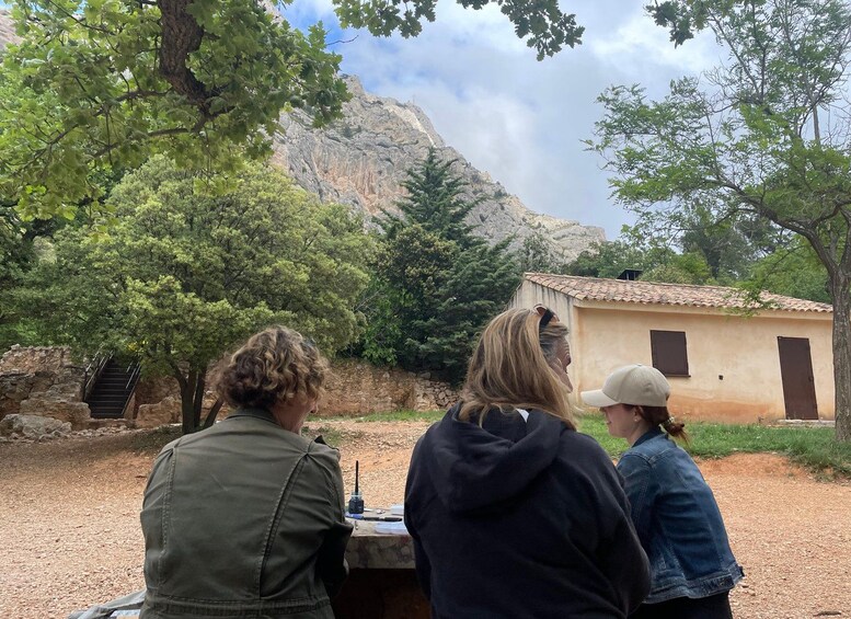 Three people sitting at a table outdoors with a mountain and a small building in the background. 4