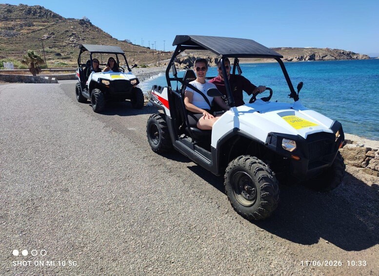 Two off-road vehicles parked by a coastal road with a rocky shoreline and a clear blue sky. 4