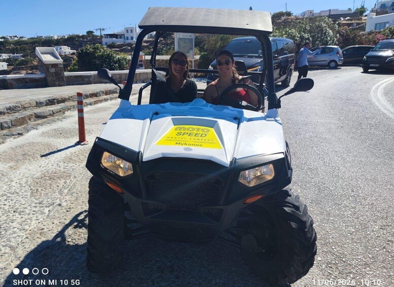 A white golf cart with a yellow sign on the front, parked on a road with buildings and vegetation in the background. 3
