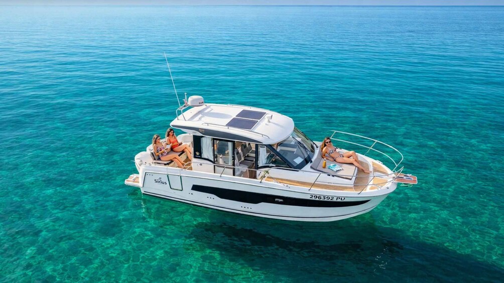 A white motorboat named 'Sirius' with two people on board, floating on clear turquoise water. 1