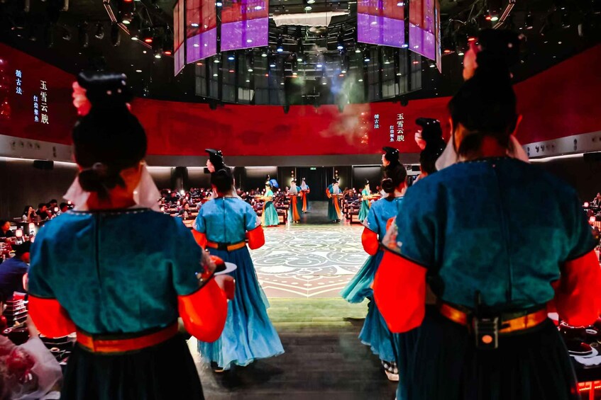 A traditional performance with performers in blue and red attire, a patterned floor, and a red backdrop with Chinese characters. 3