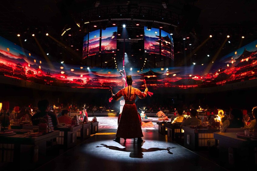 A performer in traditional attire on a stage with a backdrop of a night scene with lanterns. 4