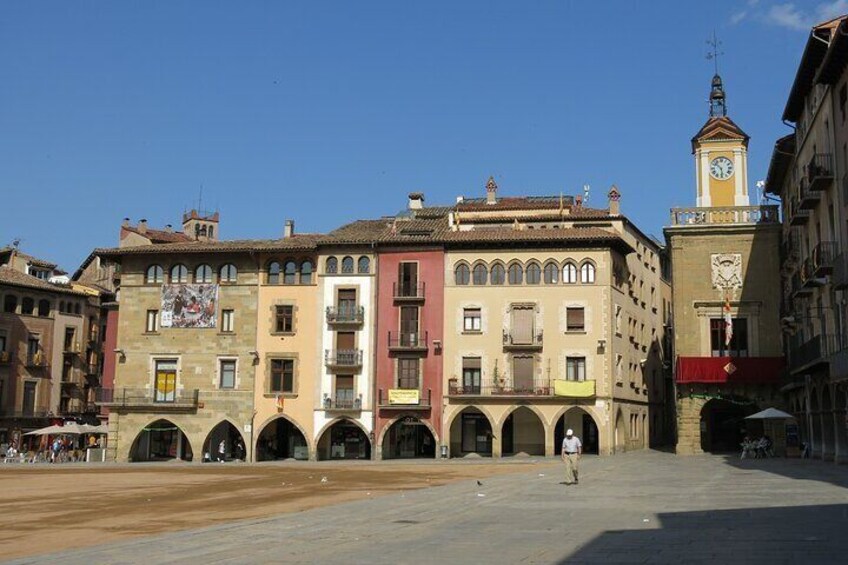 A historic square with colorful buildings, a clock tower, and a central open space. 5