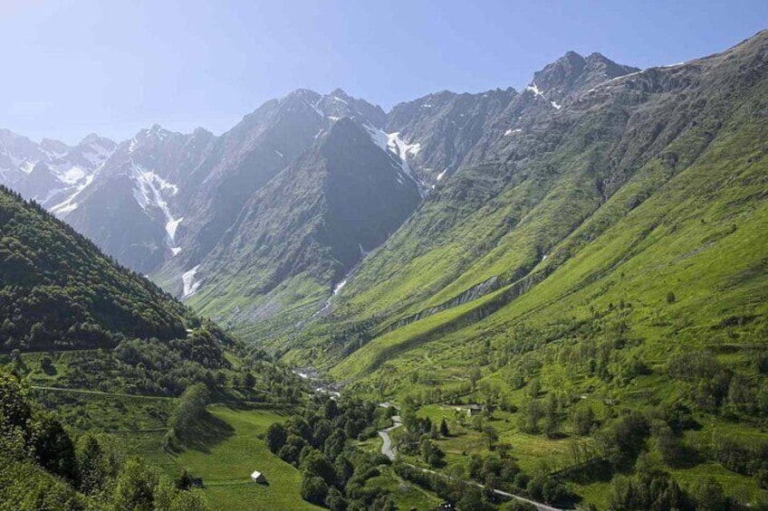 A valley with lush greenery, a winding road, and snow-capped mountains in the background. 1