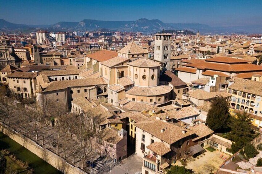 A historic cityscape with a prominent church tower, dense urban buildings, and a distant mountain range. 4