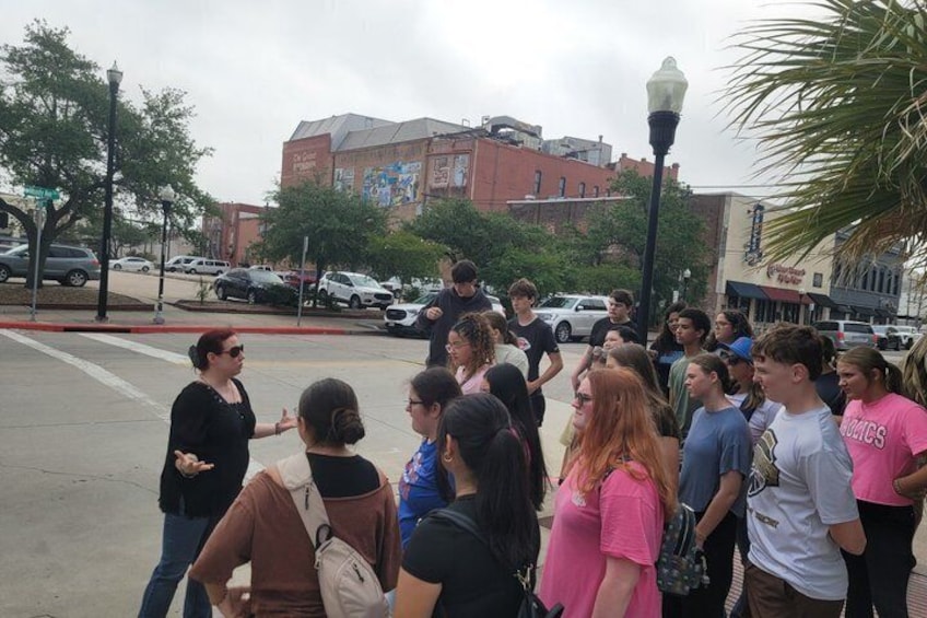 A group of people standing on a sidewalk in an urban area with buildings and parked cars in the background. 4
