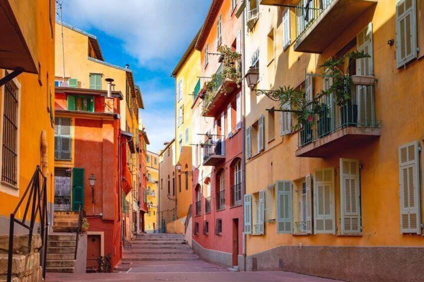 A narrow street flanked by colorful buildings with balconies and shutters. 5