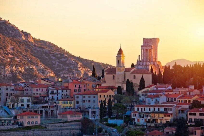 A coastal town with historic buildings, a prominent church, and a hill in the background. 1