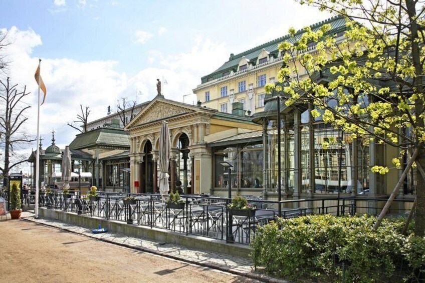A classical building with a portico, a café with outdoor seating, and a tree with yellow flowers. 5