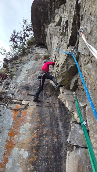 A person climbing a rocky cliff with safety ropes. 5